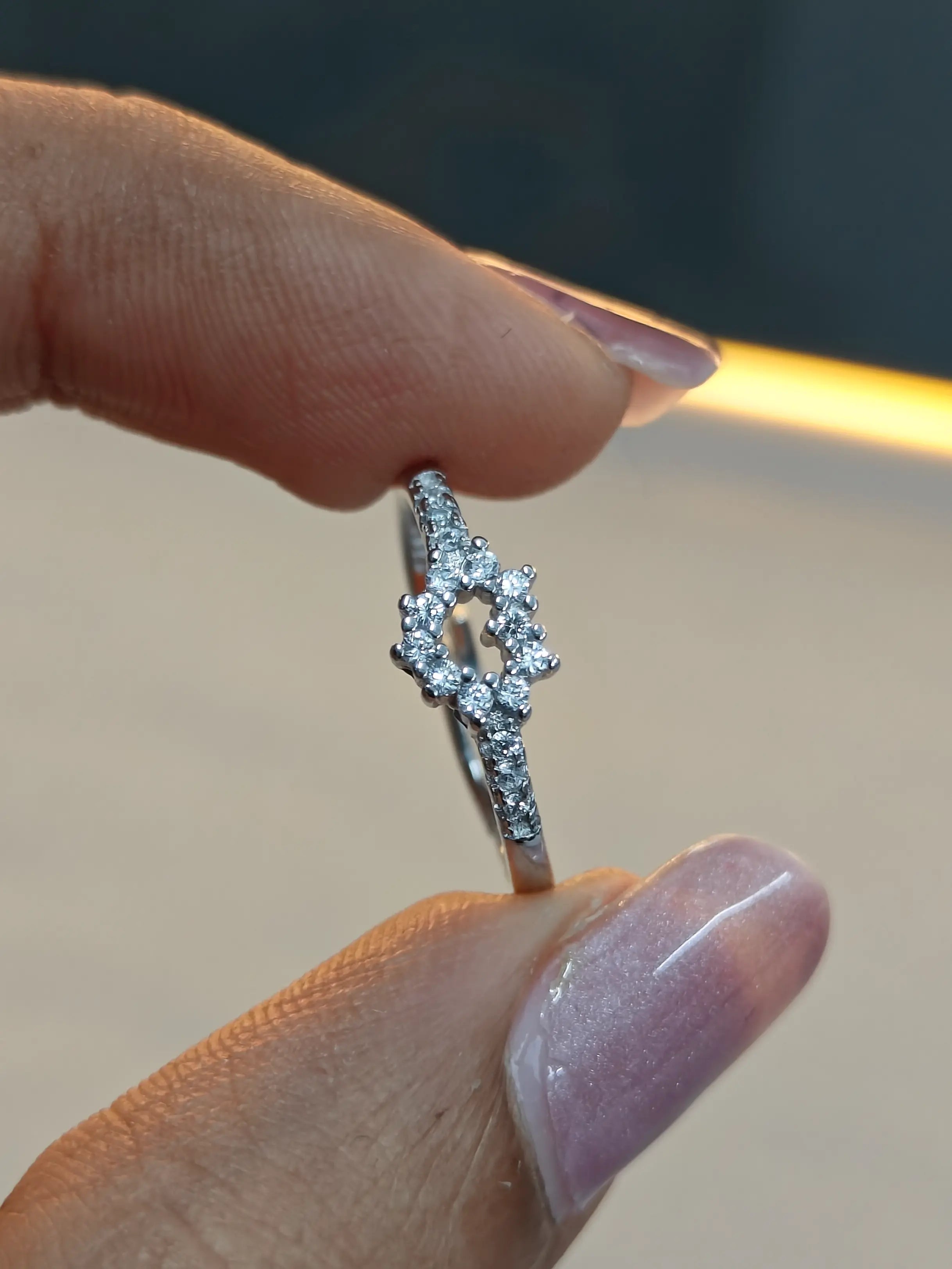 Silver ring with diamonds held between fingers against a blurred background